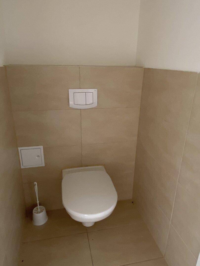 Separates WC mit wandhängender Toilette und beigefarbenen Fliesen an Wänden und Boden.