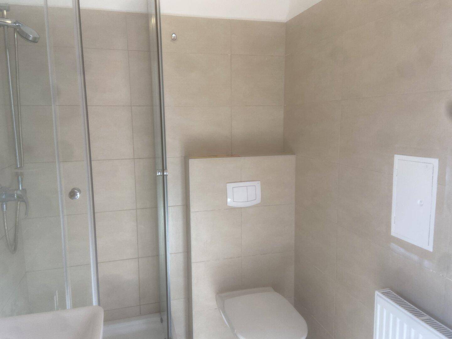 Modernes Badezimmer mit beigefarbenen Fliesen, Duschkabine und wandhängendem WC.
