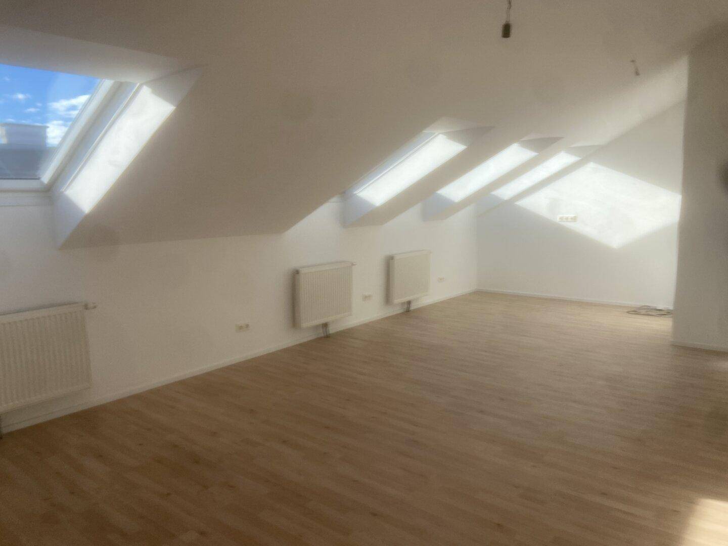Heller Wohnraum im Dachgeschoss mit Schrägdach, mehreren Dachfenstern und Laminatboden.