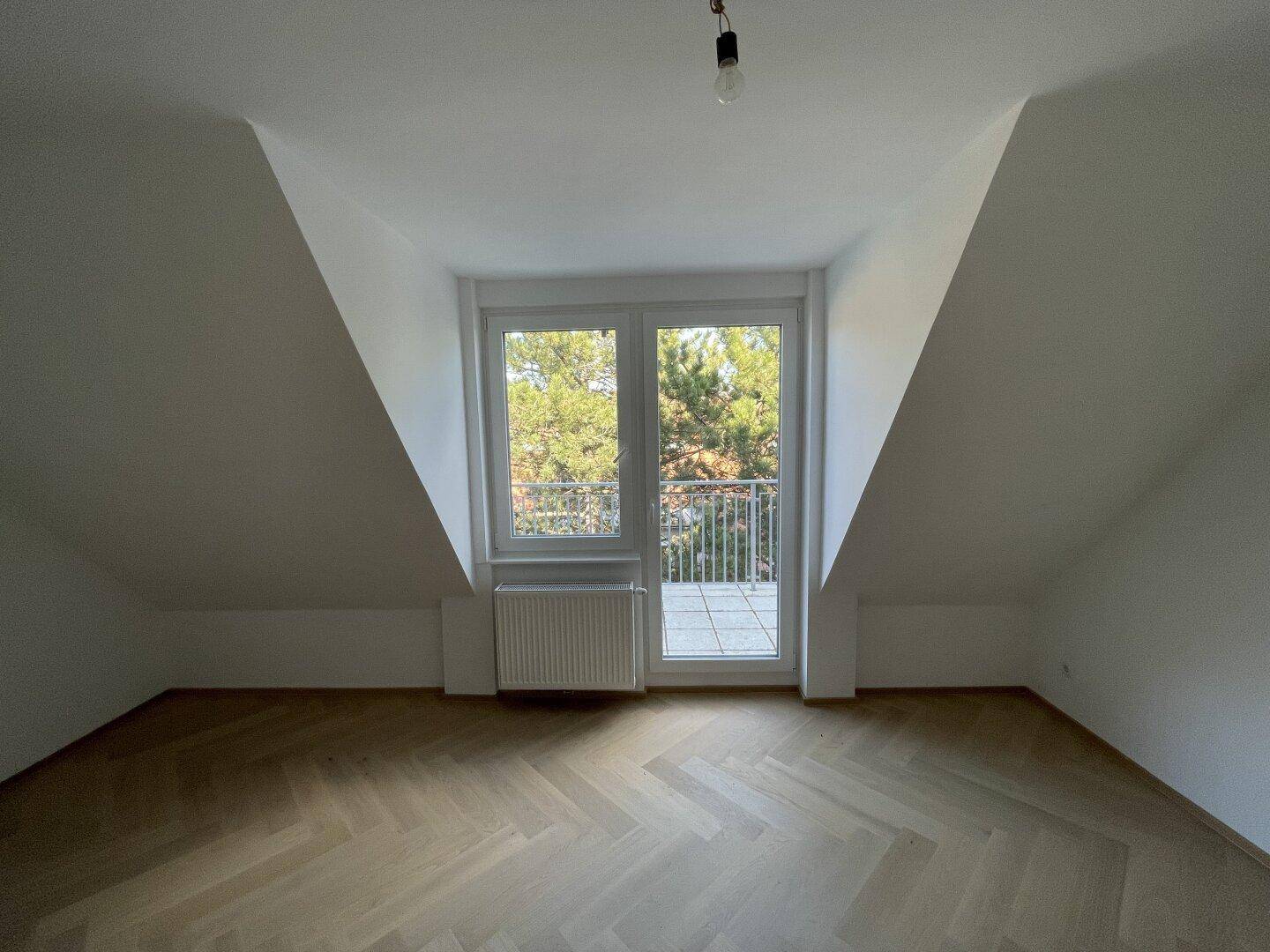 Heller Raum mit Fischgrätparkett und Zugang zu einer kleinen Terrasse oder Balkon.