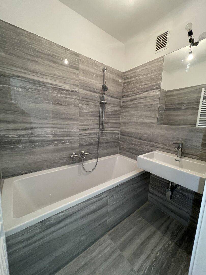 Modernes Badezimmer mit grauen Fliesen, Badewanne und Waschbecken.