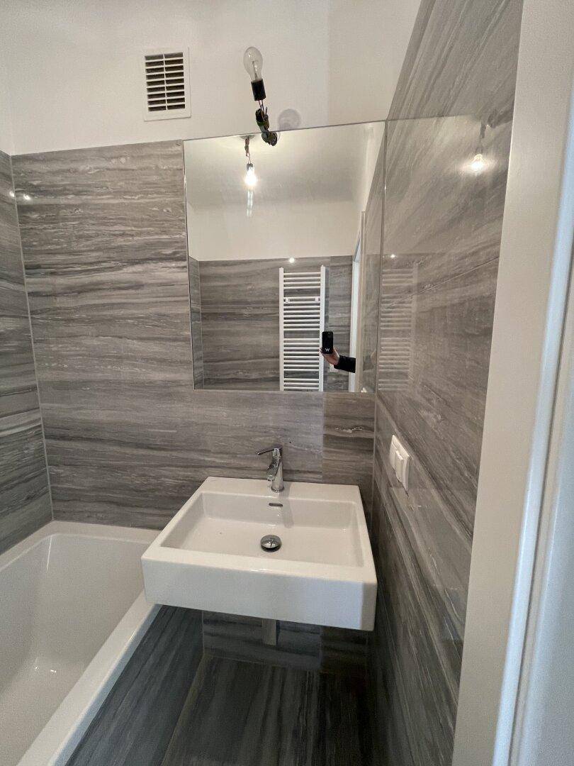 Modernes Badezimmer mit schwebendem Waschbecken, großem Spiegel und grauen Fliesen.