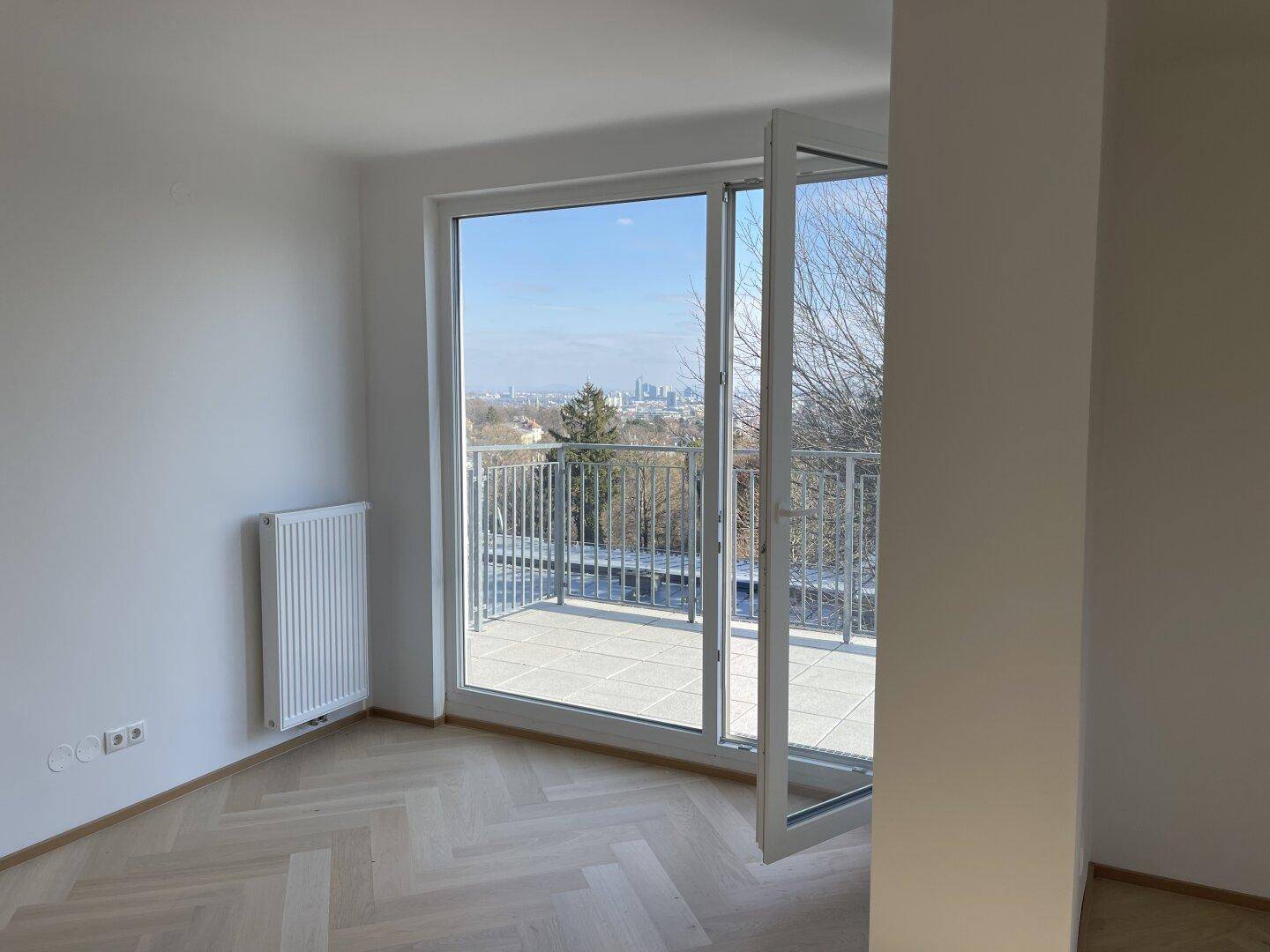 Heller Raum mit Fischgrätparkett und großem Fenster mit Zugang zur Terrasse.