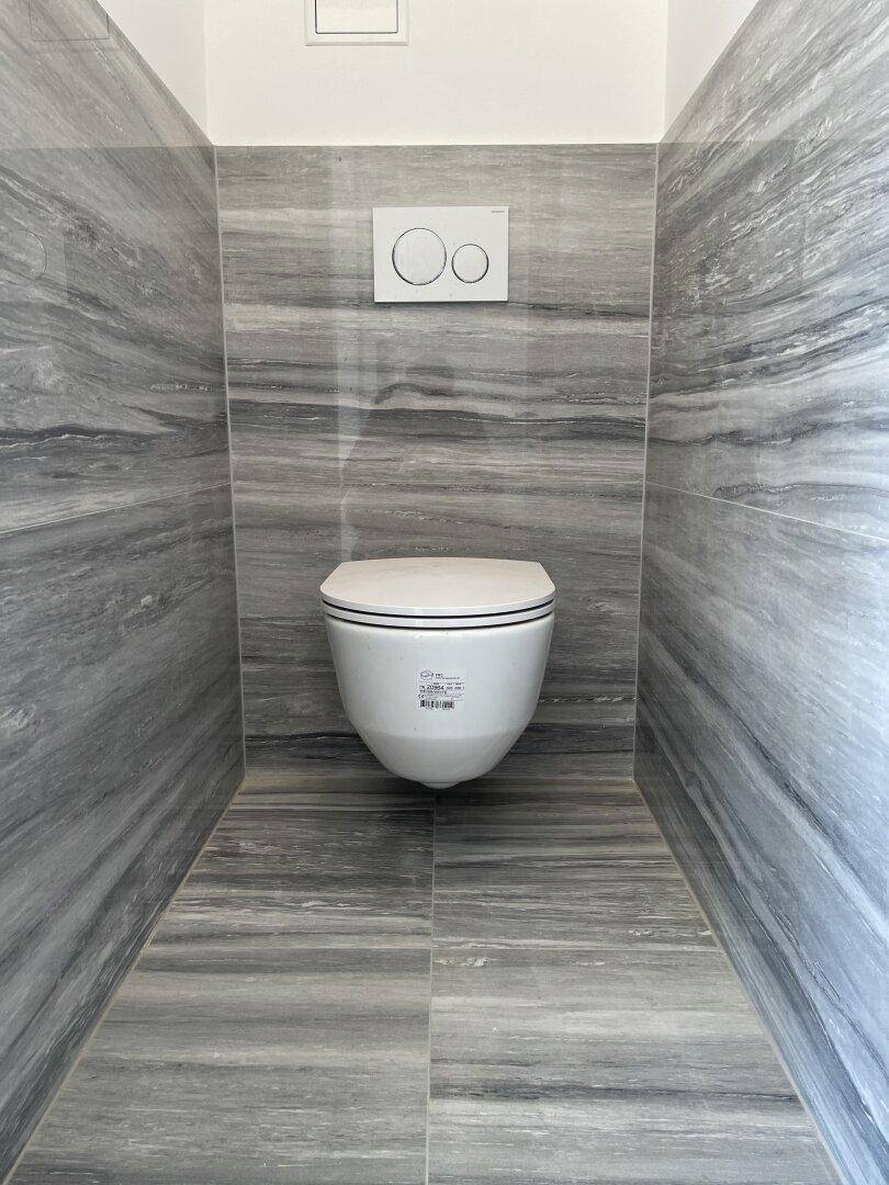 Separate Toilette mit wandhängendem WC und modernen grauen Fliesen.