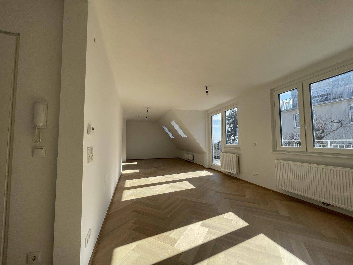 Lichtdurchfluteter Raum mit Fischgrätparkett, Dachfenstern und Zugang zum Balkon.