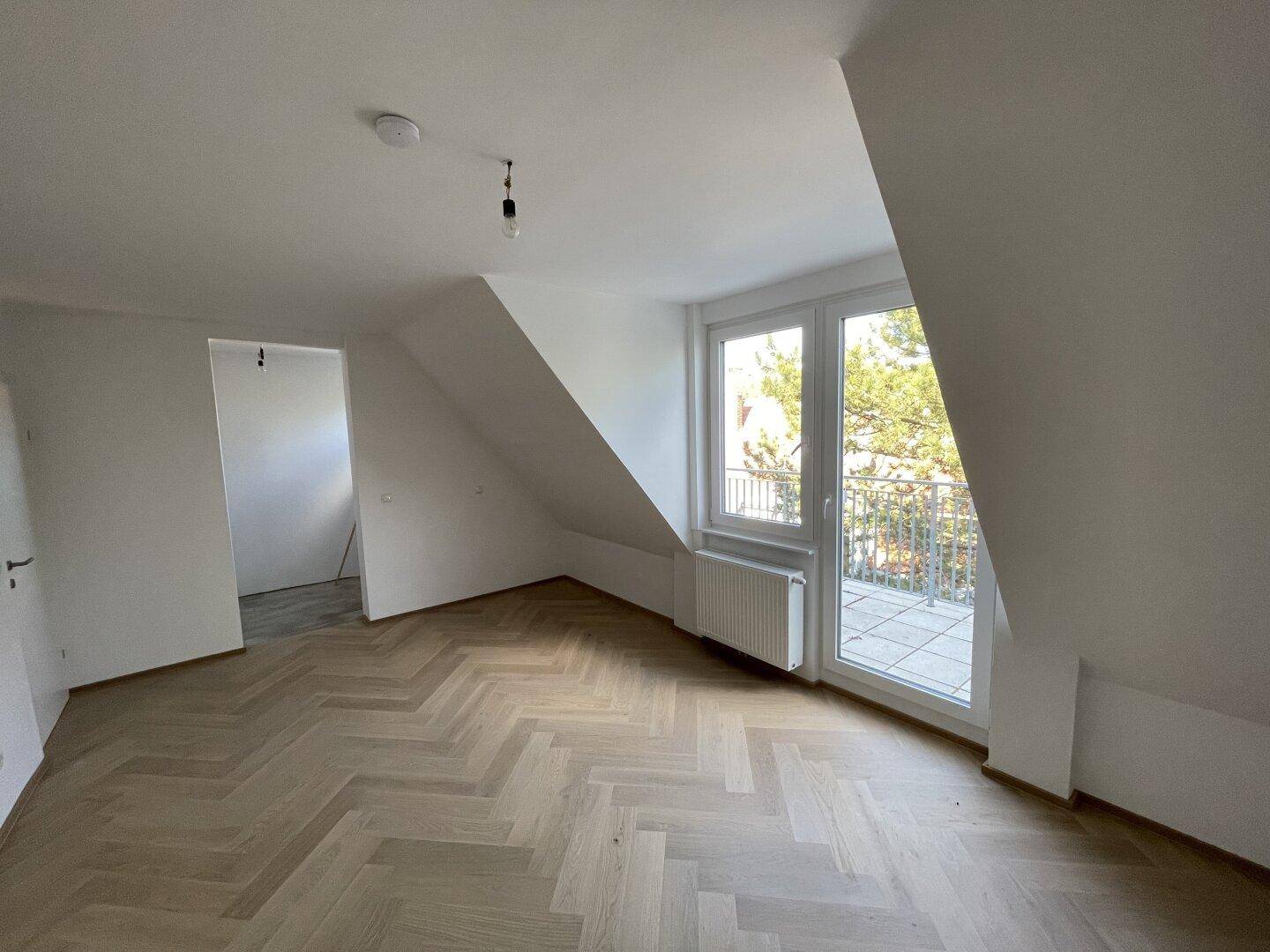 Heller Raum mit Dachschräge, Fischgrätparkett und Zugang zu einer Außenterrasse.