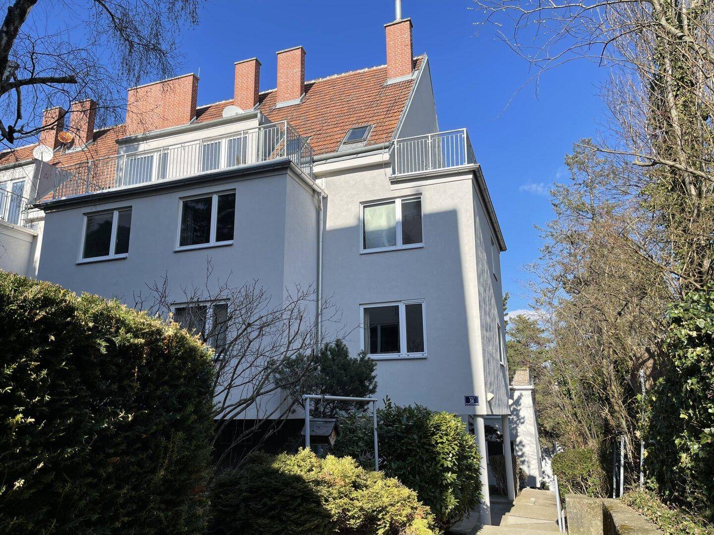Modernes Mehrfamilienhaus mit weißer Fassade, Terrassen und gepflegter Hecke.