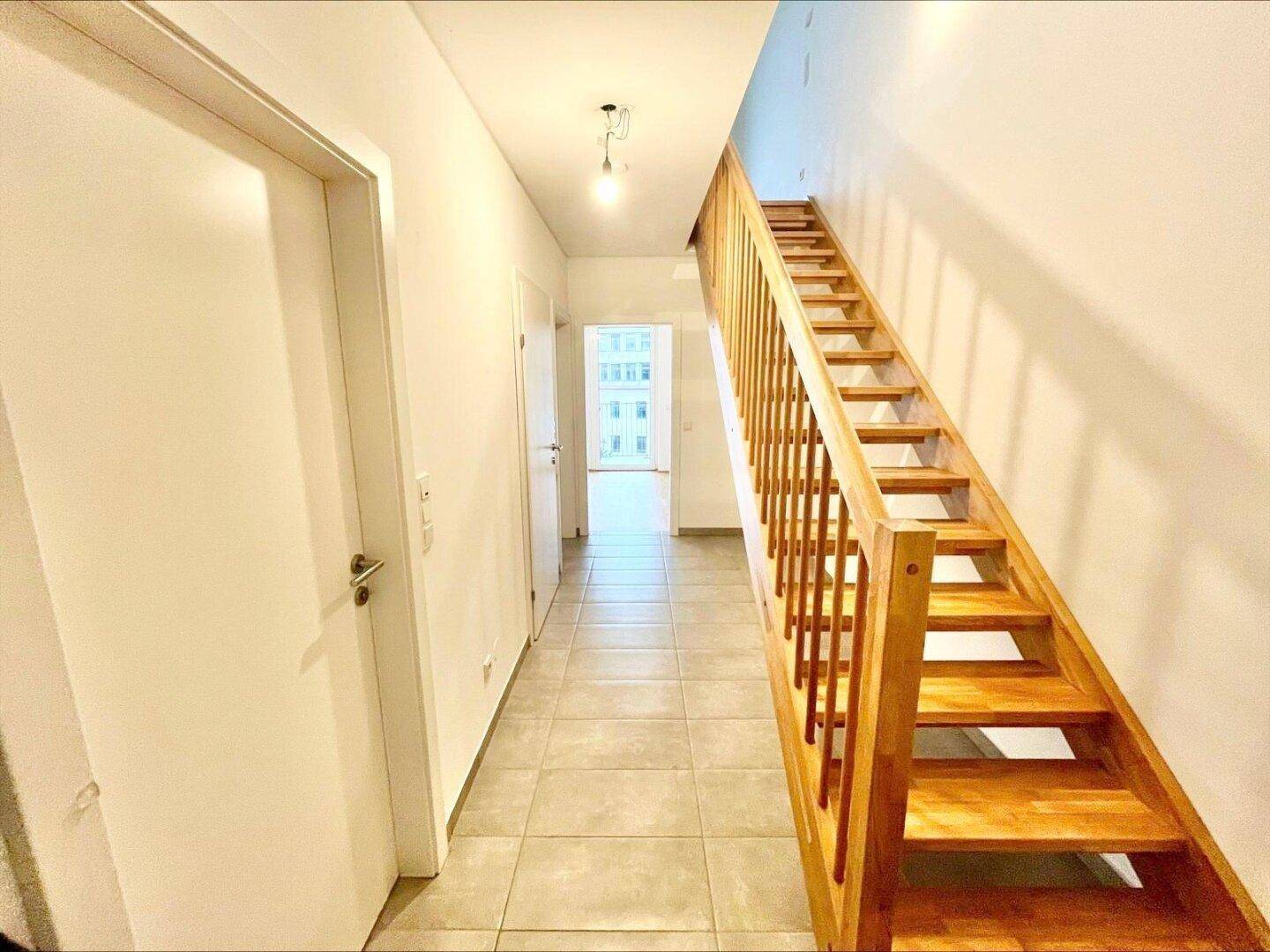 Heller Flur mit Holztreppe und Fliesenboden, der zu weiteren Räumen führt.