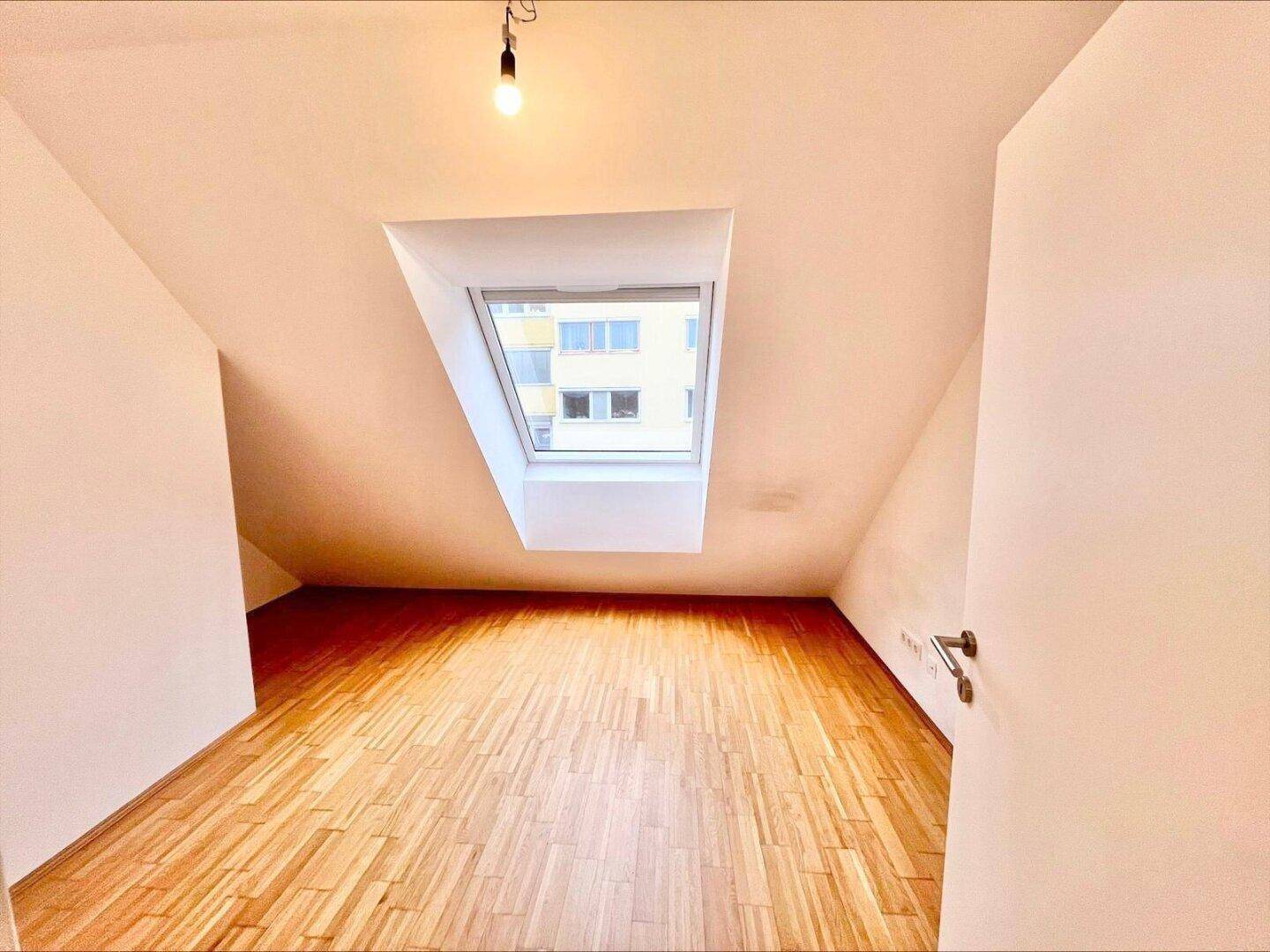 Dachgeschosszimmer mit Holzboden, Dachschräge und großem Dachfenster für viel Tageslicht.