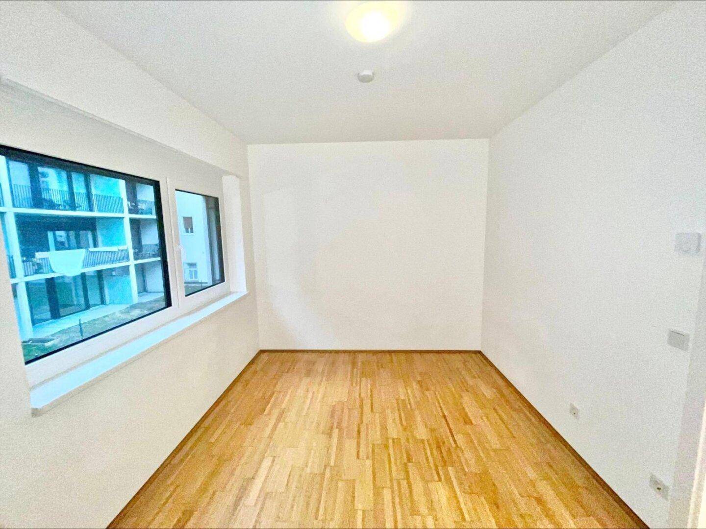 Leeres Zimmer mit Parkettboden und großem Fenster, das einen Blick auf die Umgebung bietet.