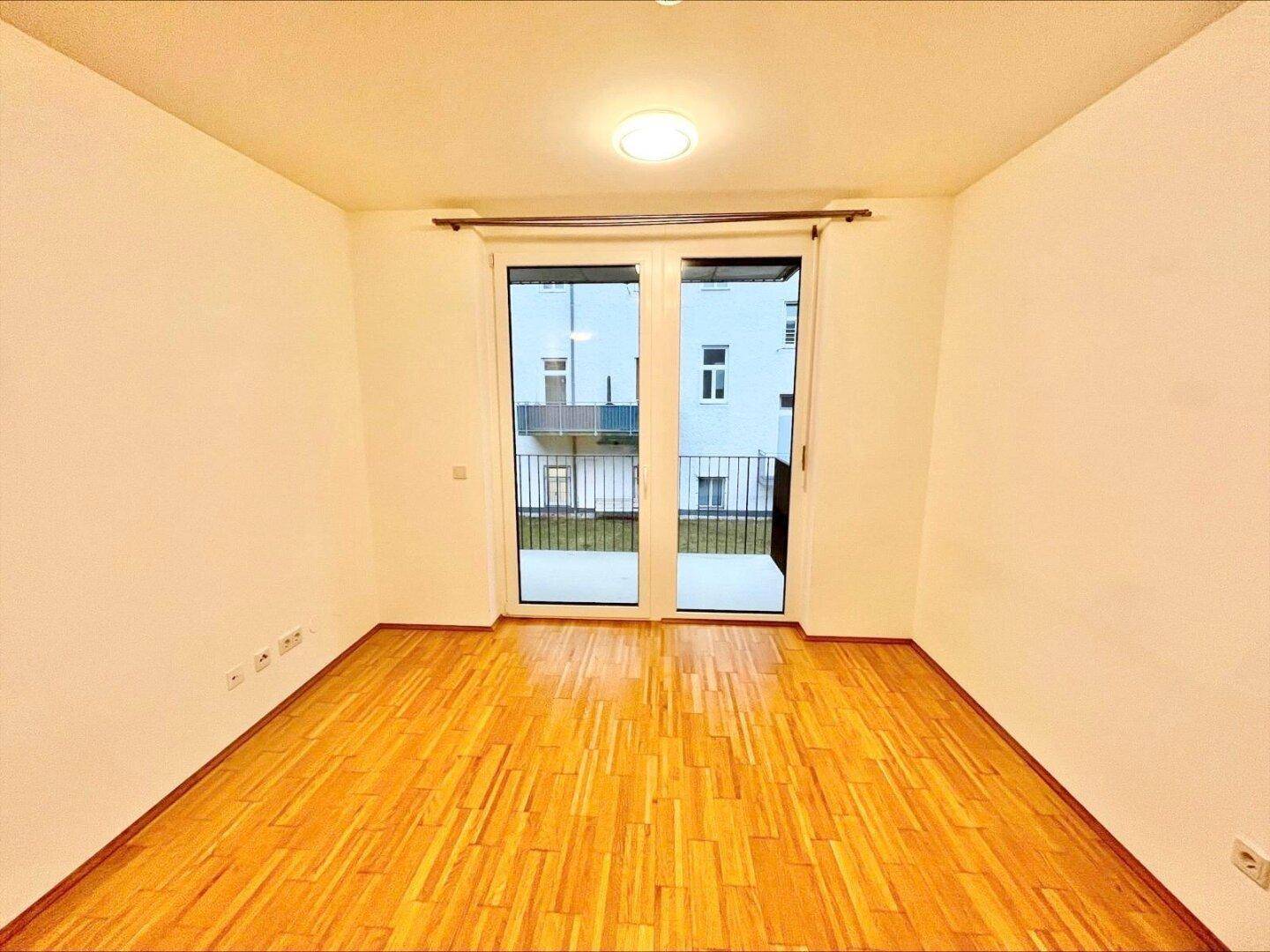 Helles Zimmer mit Parkettboden und einer Glastür, die Zugang zu einem Außenbereich ermöglicht.