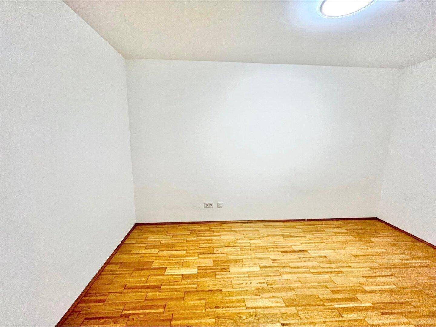 Geräumiges, leeres Zimmer mit hellem Parkettboden und weißen Wänden, bereit zur Einrichtung.
