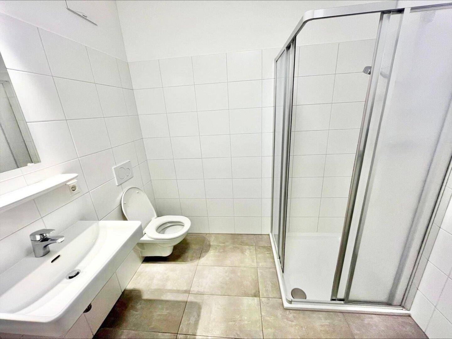 Modernes Badezimmer mit weißen Wandfliesen, Duschkabine, WC und Waschbecken.