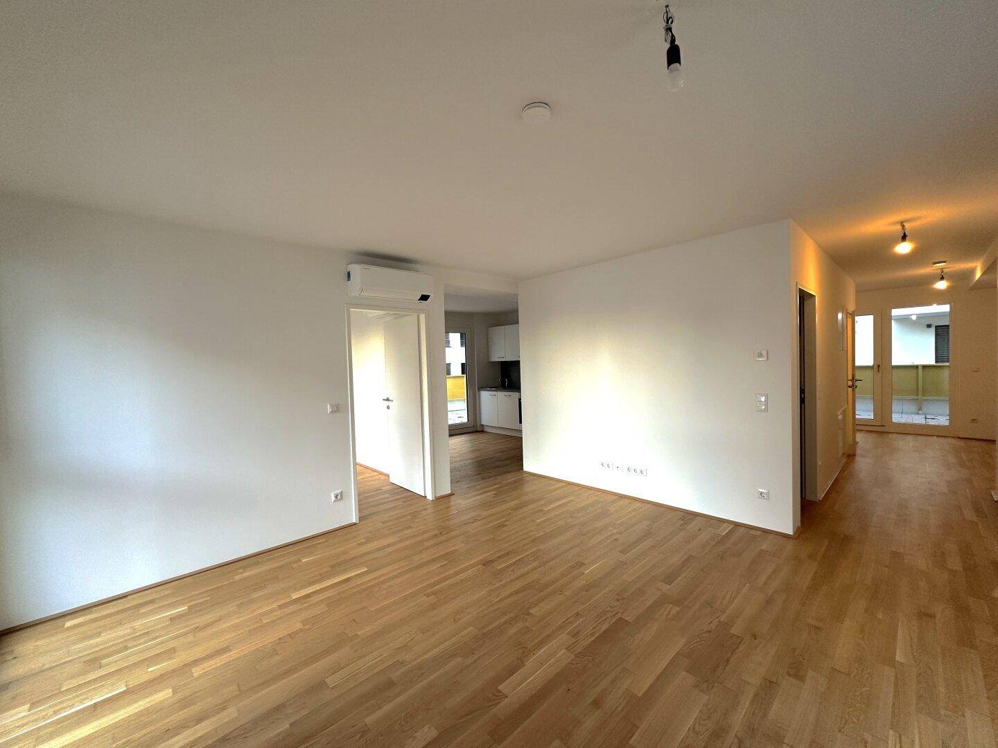 Heller Wohnbereich mit durchgehendem Holzboden, der zu weiteren Räumen und der Küche führt.
