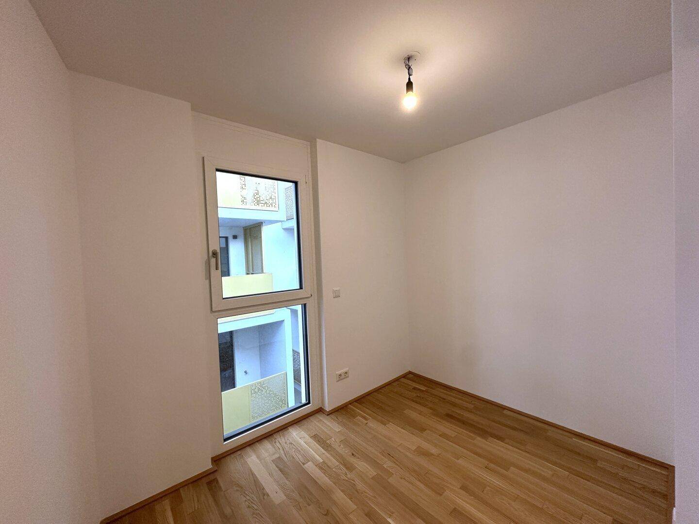 Ruhiges Zimmer mit Holzboden und großem Fenster, das einen Blick auf den Innenhof bietet.