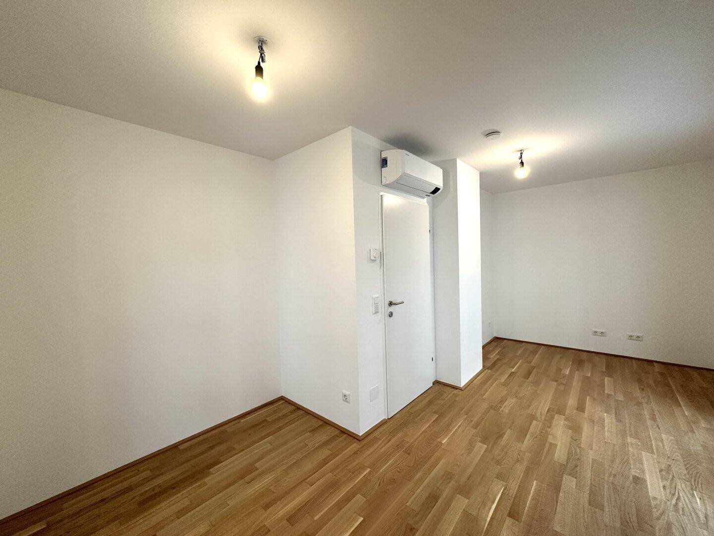 Geräumiges Zimmer mit Holzboden und Klimaanlage, ideal als Schlaf- oder Arbeitszimmer nutzbar.