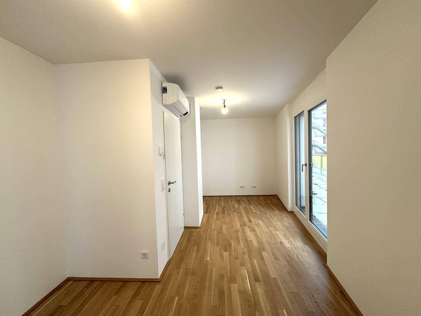 Helles Zimmer mit Holzboden, großen Fenstern und Klimaanlage, bietet Komfort und viel Licht.