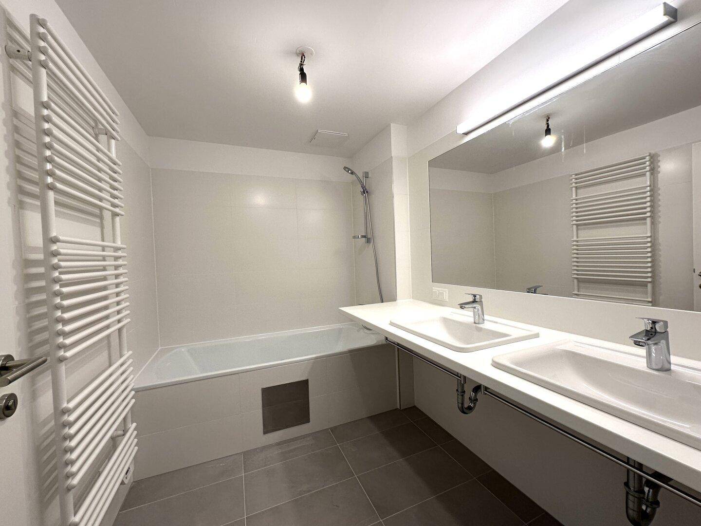 Modernes Badezimmer mit Badewanne, Doppelwaschbecken, großem Spiegel und beheiztem Handtuchhalter.