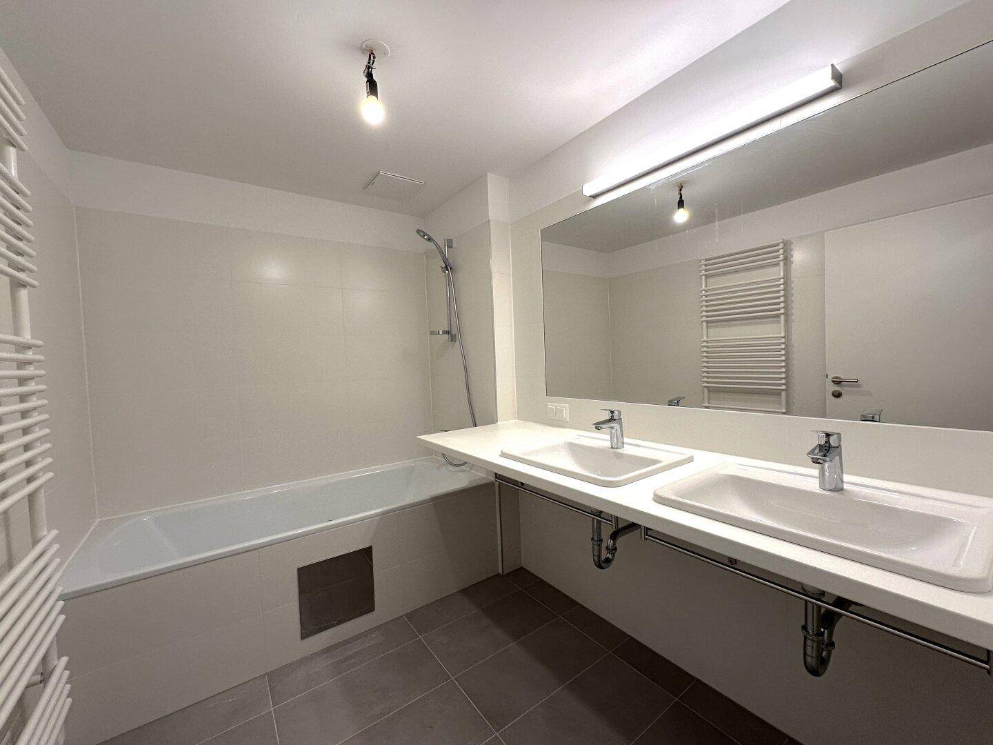 Geräumiges Badezimmer mit Doppelwaschbecken, großem Spiegel und Badewanne, in modernem Design.