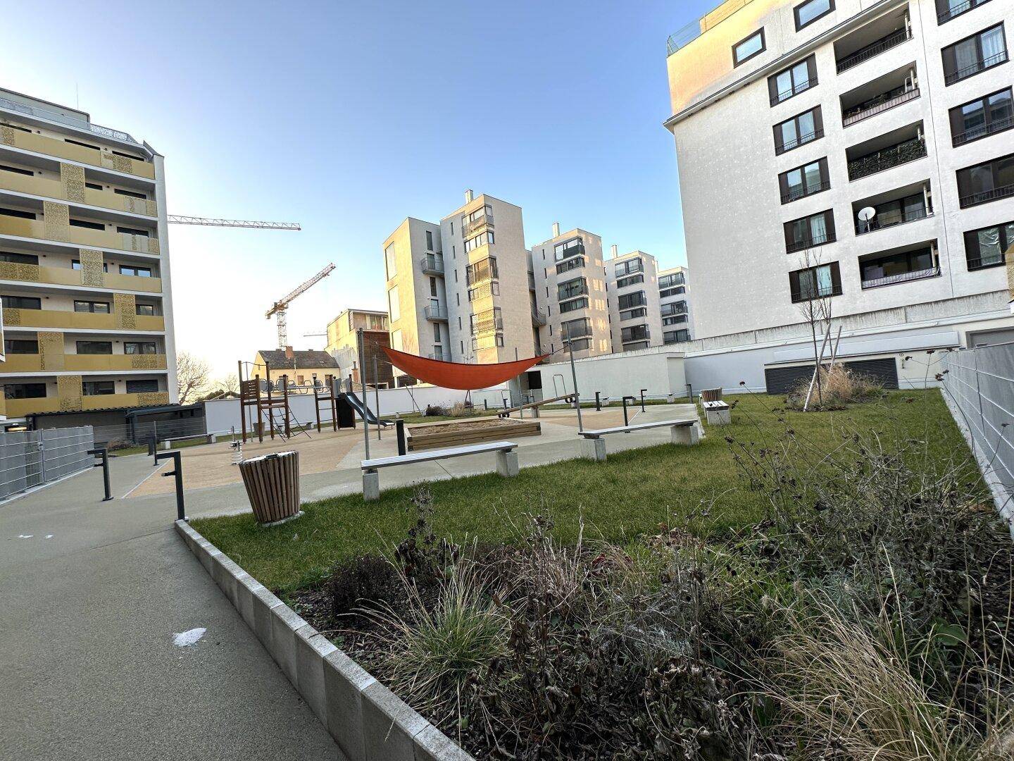 Außenansicht eines modernen Wohnkomplexes mit Spielplatz und begrünten Gemeinschaftsflächen.