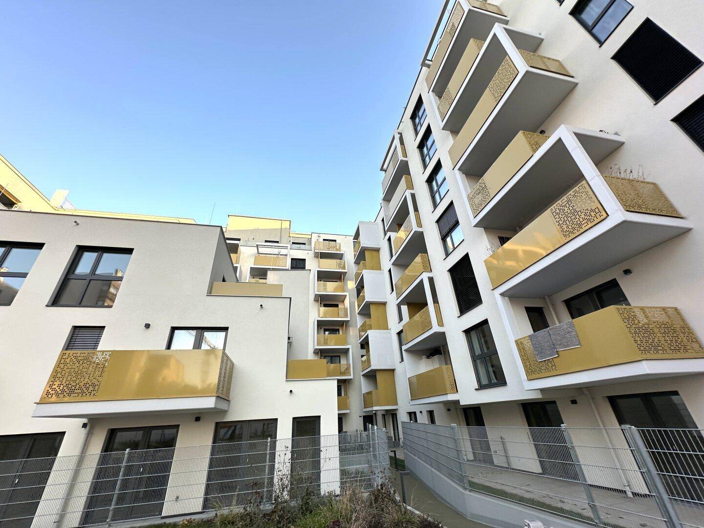 Moderne Gebäudefassade mit zahlreichen Balkonen und gelben Akzenten unter blauem Himmel.