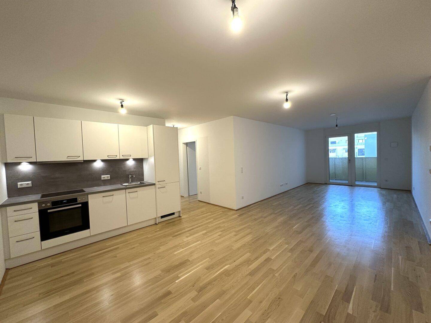 Geräumiger Wohn-Essbereich mit moderner Küchenzeile und Zugang zu einem Balkon.