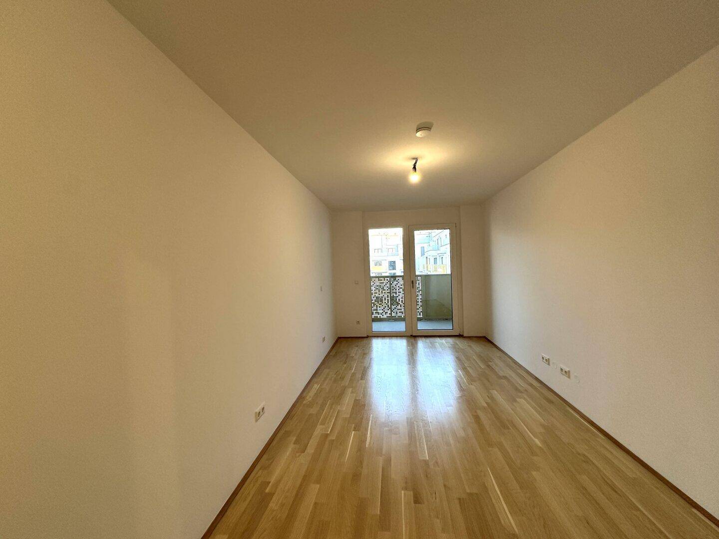Heller Raum mit Parkettboden und Balkonzugang, bietet viel Potenzial für persönliche Einrichtungsideen.
