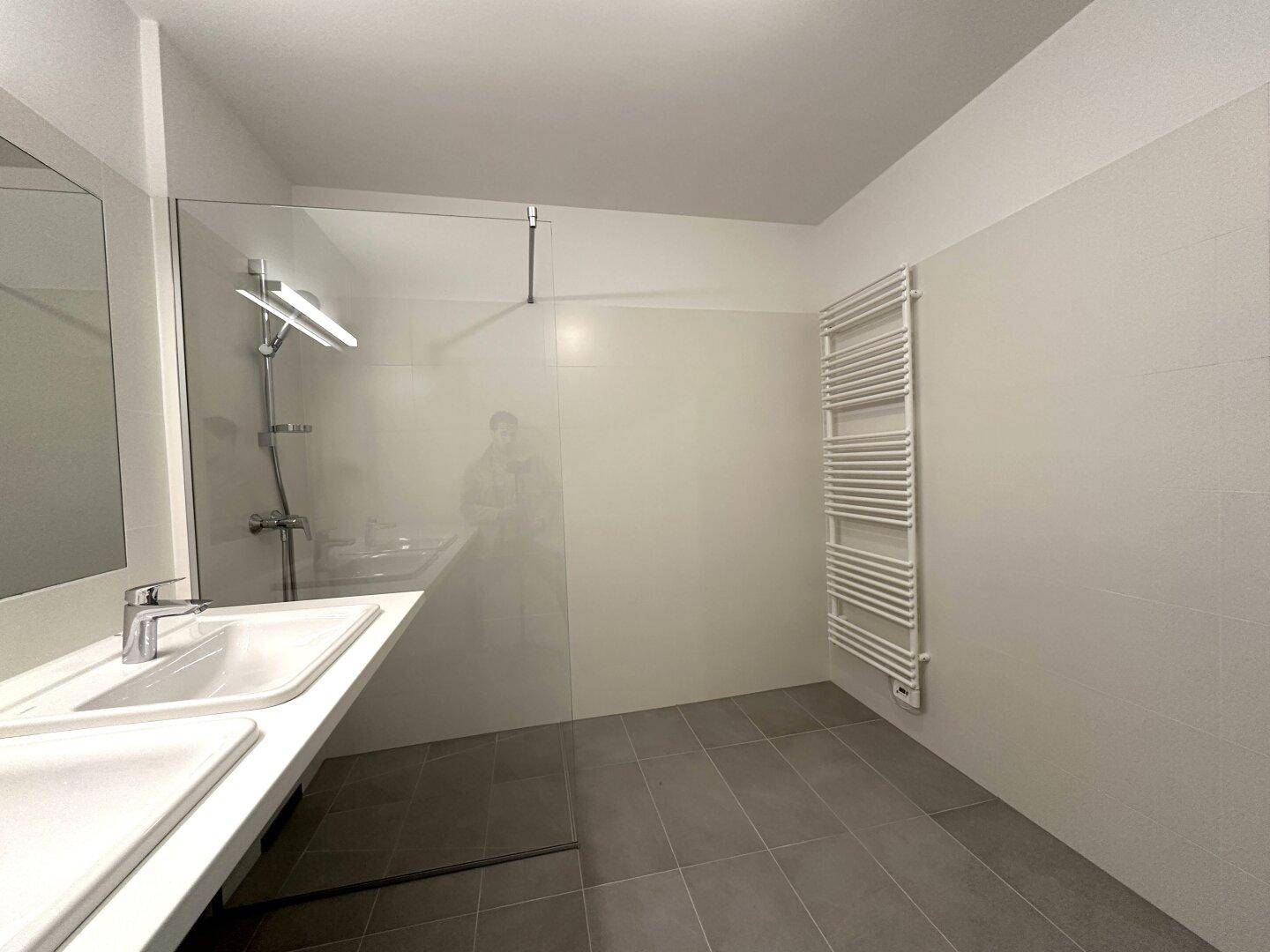 Begehbare Dusche mit Glaswand und praktischem Handtuchheizkörper im modernen Badezimmer.