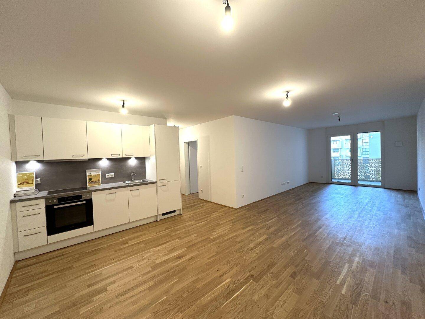 Heller offener Wohnbereich mit integrierter Küche und Zugang zu einem Balkon.