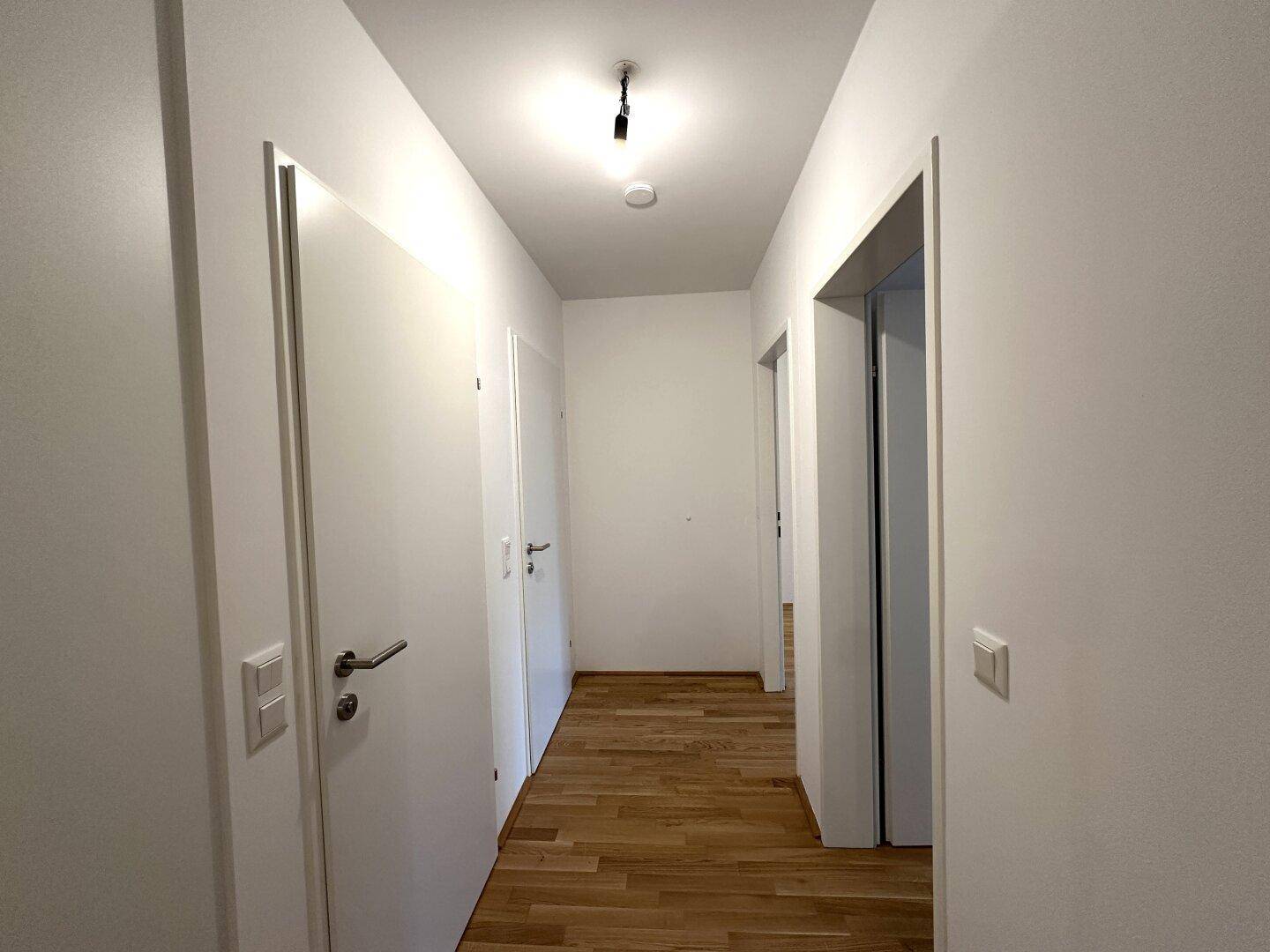 Langer, heller Flur mit Holzboden und mehreren Türen zu den Zimmern.