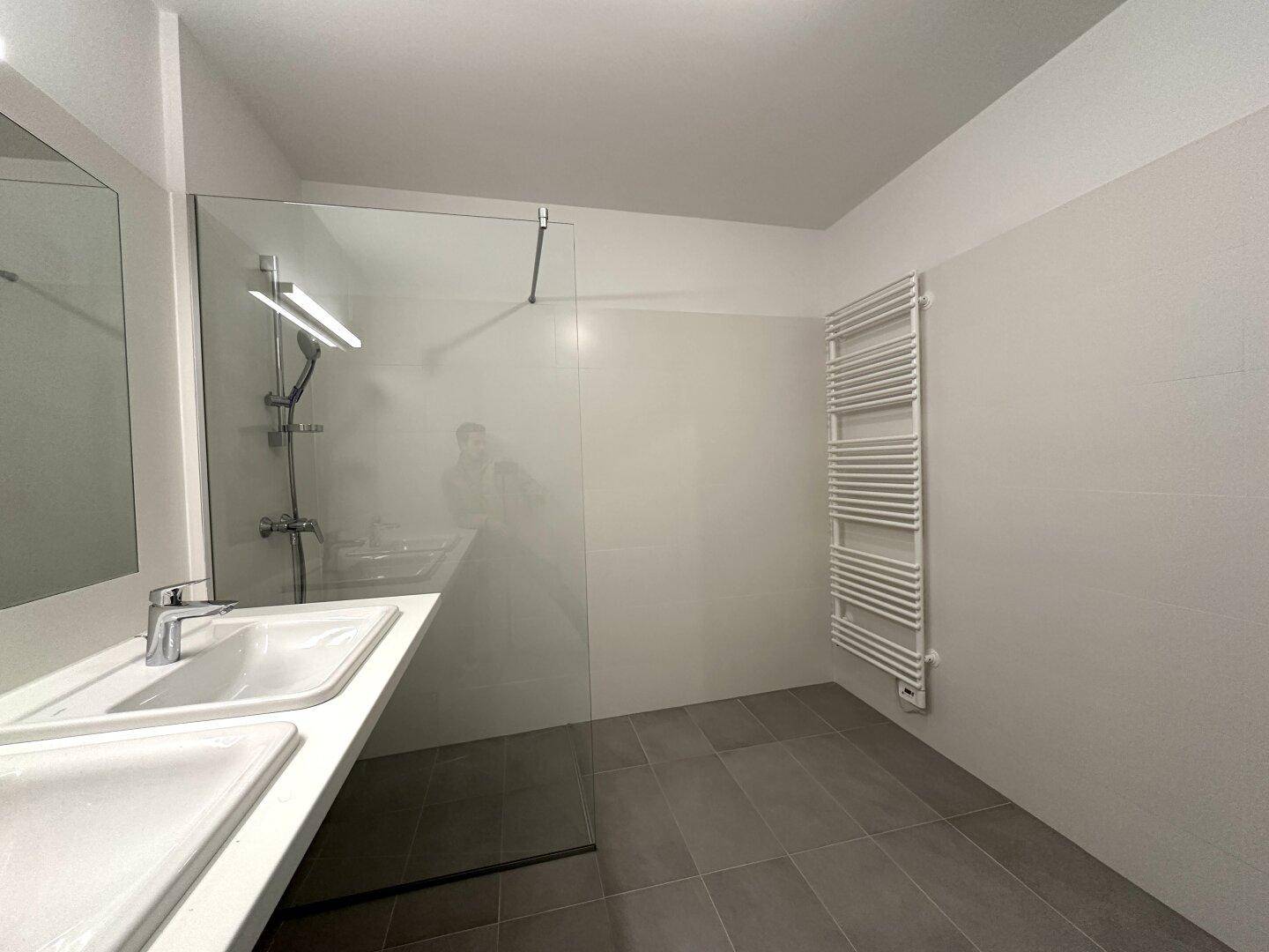 Begehbare Dusche mit Glaswand und beheiztem Handtuchhalter in modernem Badezimmer.