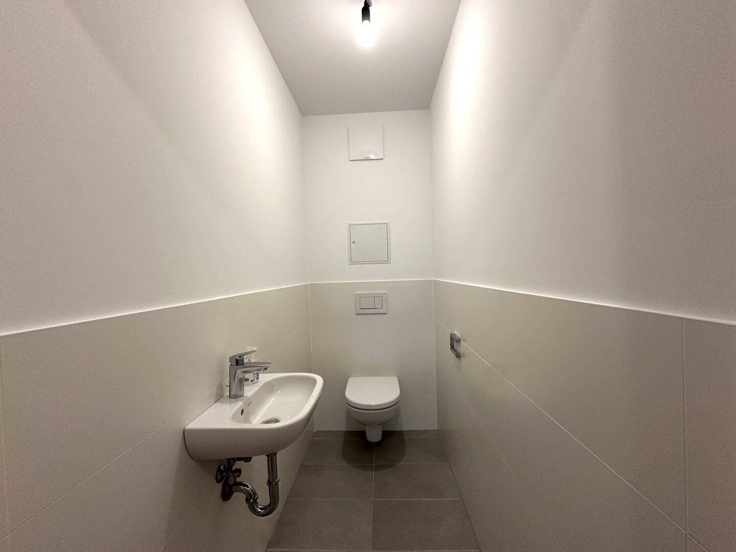Helles Gäste-WC mit wandhängendem WC und kleinem Waschbecken, funktional und sauber.