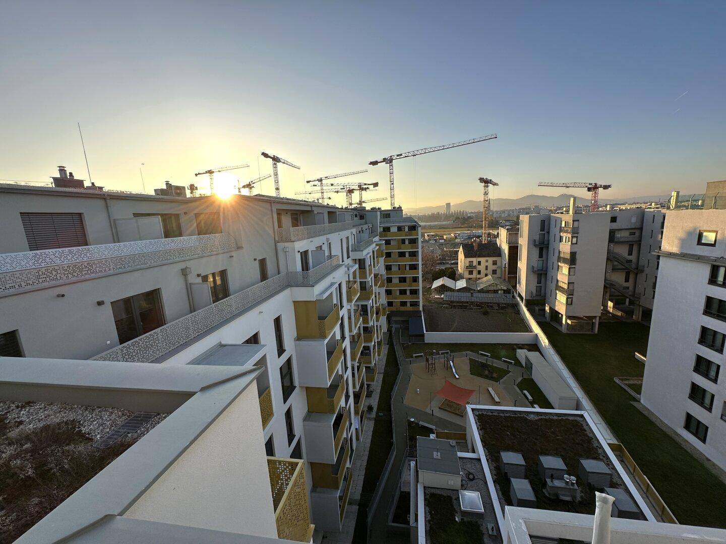 Panoramablick über eine moderne Stadtlandschaft mit neuen Wohngebäuden und Baukränen im Sonnenlicht.