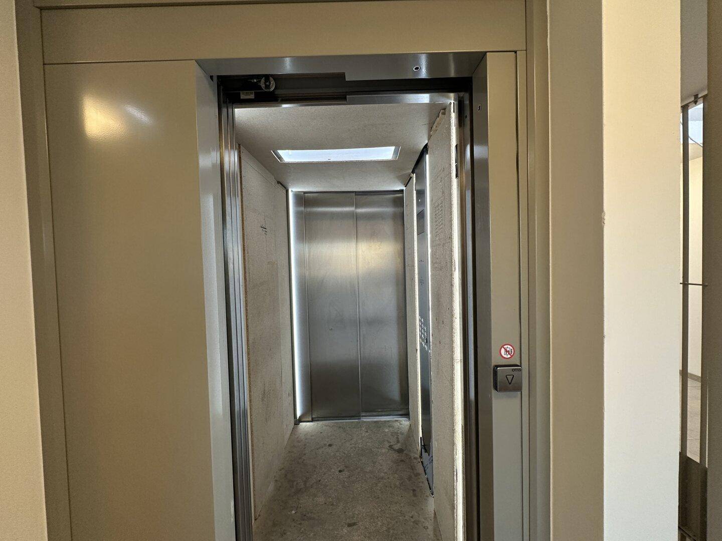 Offene Aufzugstür, die das Innere der Kabine mit Metallwänden und Deckenlicht zeigt.