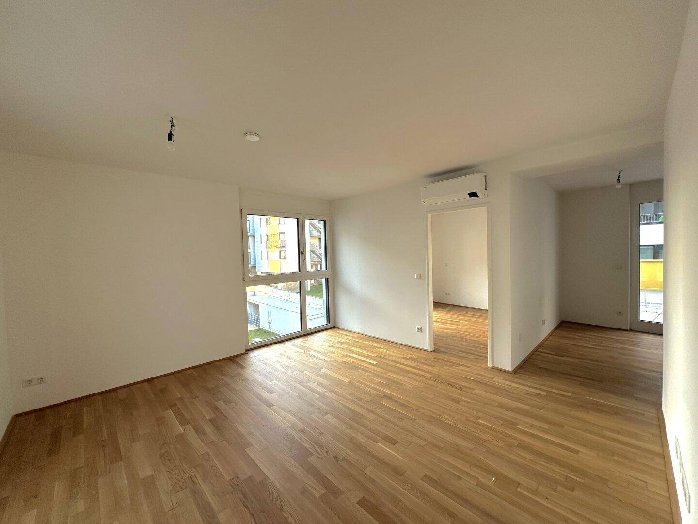 Helles, leeres Wohnzimmer mit Holzboden und großen Fenstern, bereit zum Einzug.