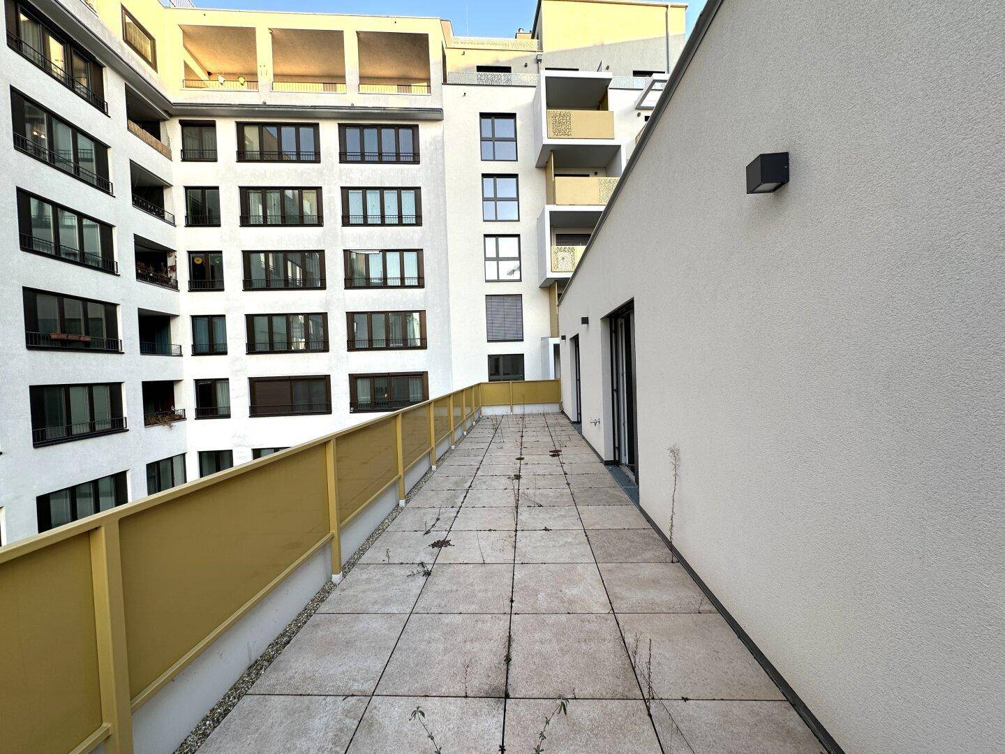 Große, geflieste Terrasse mit gelbem Geländer und Blick auf umliegende Gebäude.