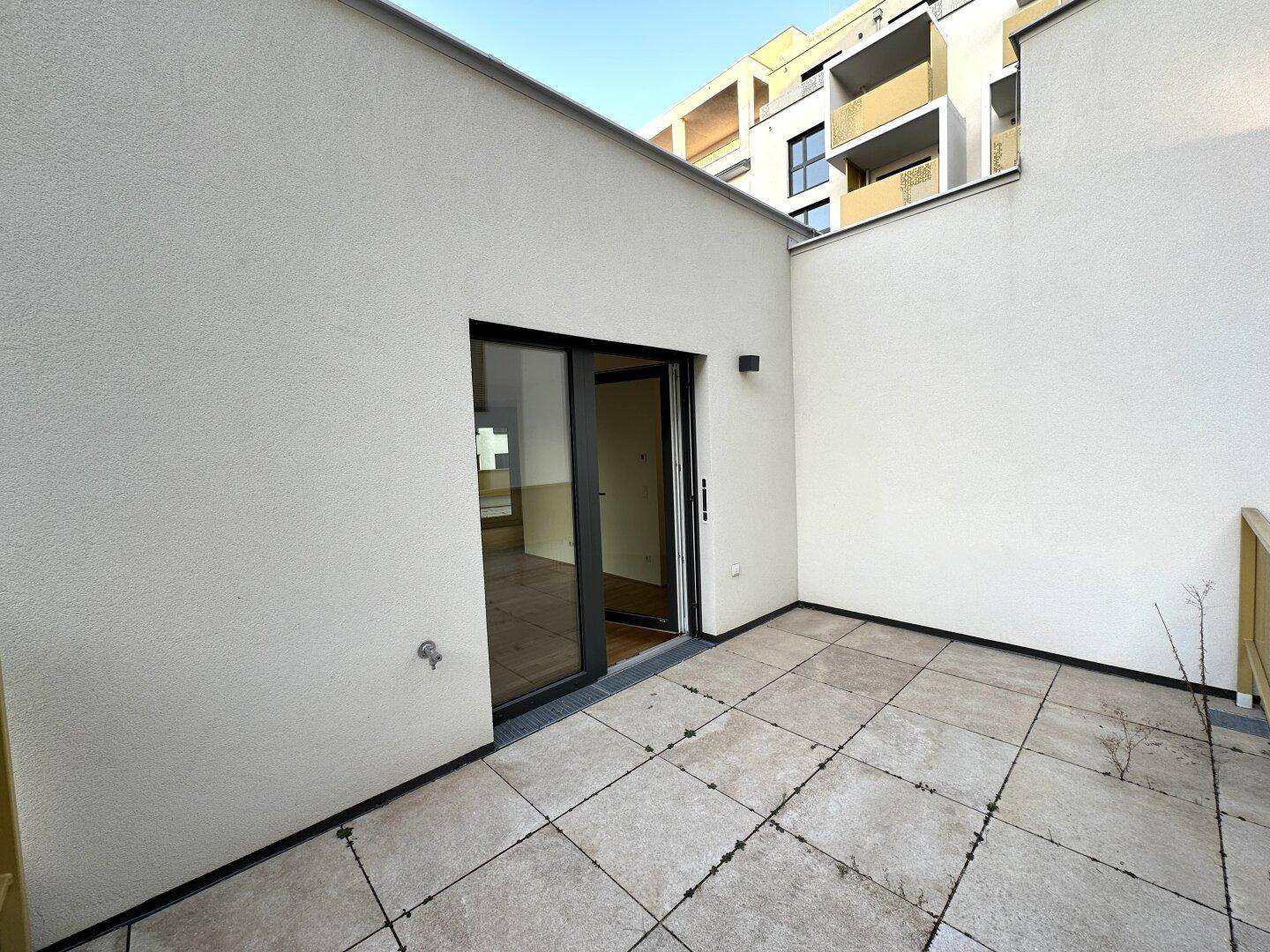 Eckterrasse mit Fliesenboden und direktem Zugang zu einem hellen Innenraum.