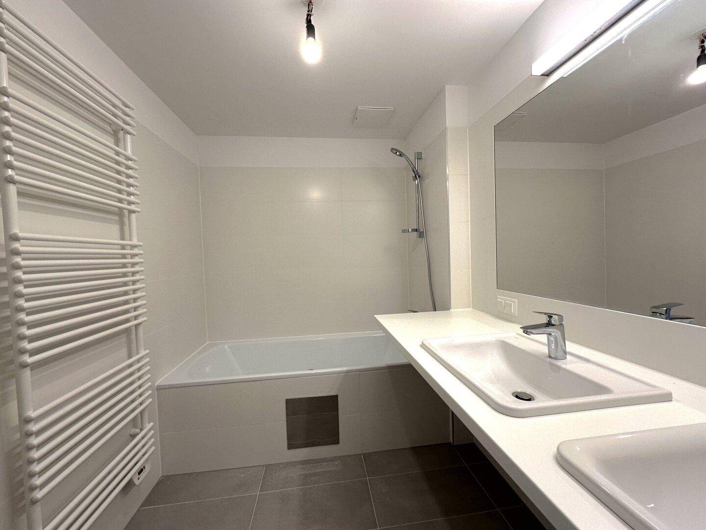 Helles Badezimmer mit Badewanne, Waschbecken und großem Spiegel, modern gefliest.