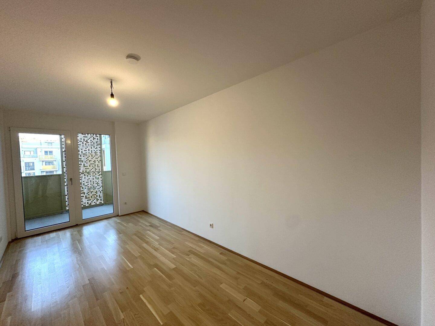 Schlafzimmer mit Holzboden, weißen Wänden und direktem Zugang zum Balkon.