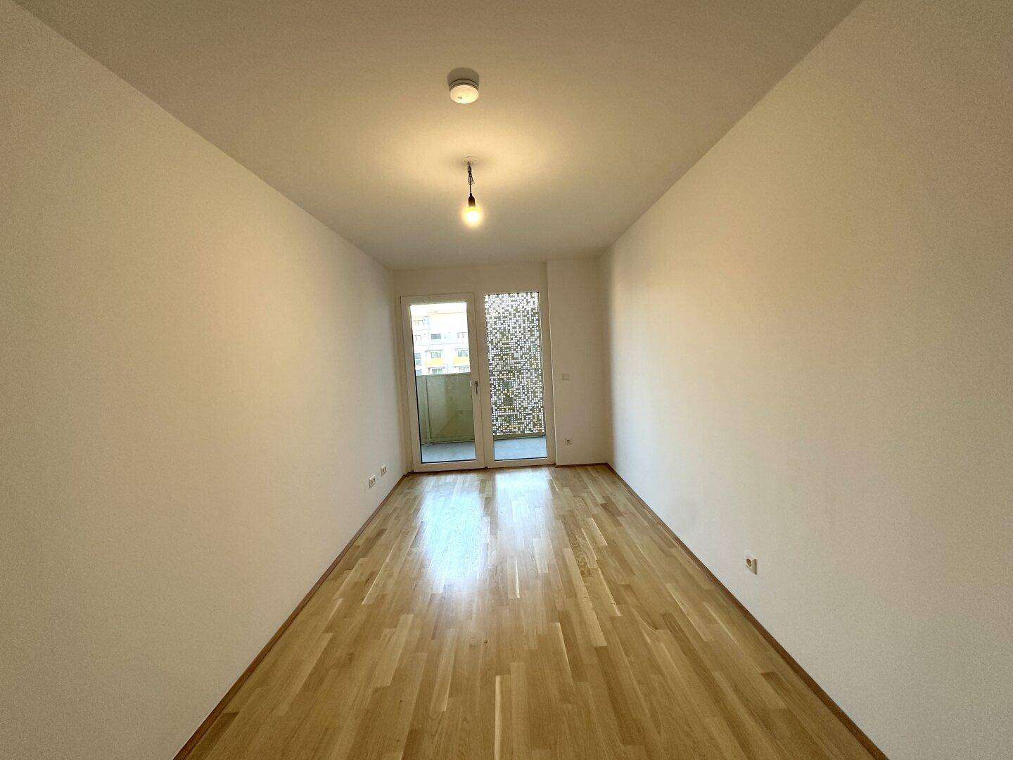 Helles Schlafzimmer mit Holzboden und Balkontür, bereit zur Einrichtung.