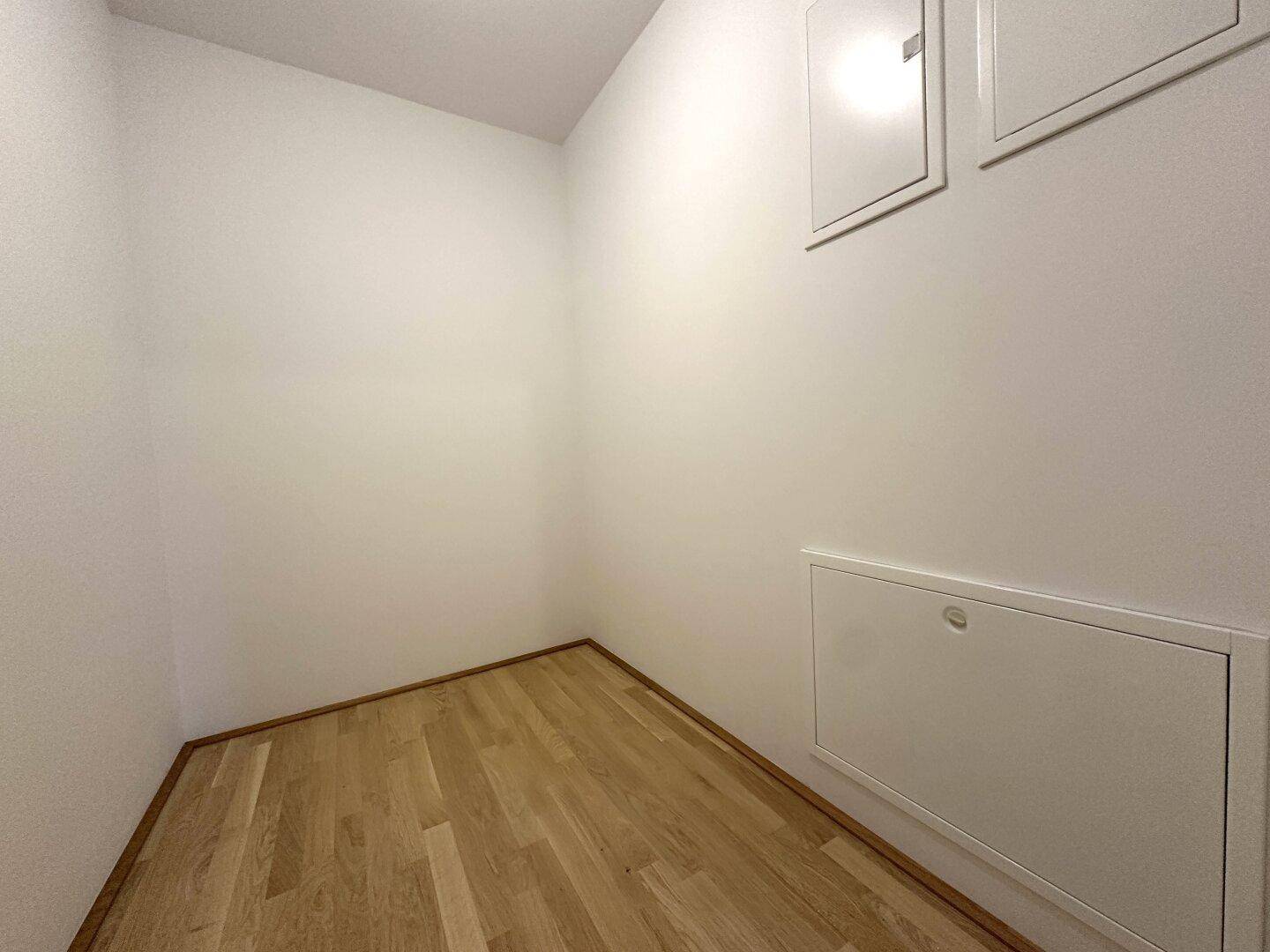 Praktischer Abstellraum mit Holzboden und weißen Wänden für zusätzlichen Stauraum.