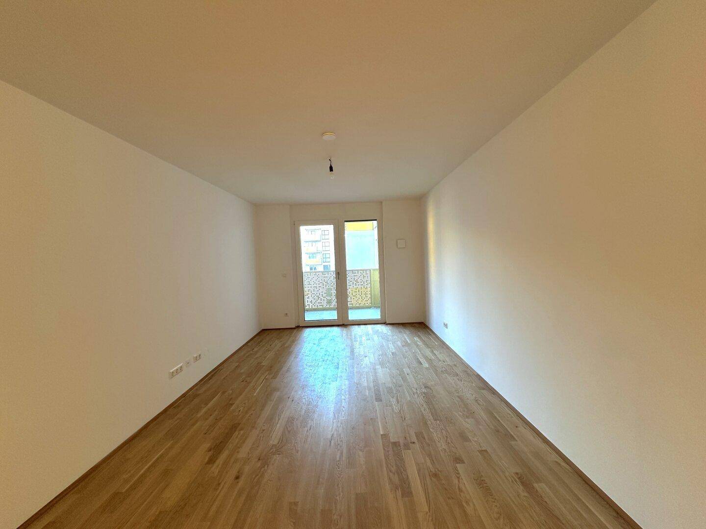 Heller Raum mit Parkettboden und Zugang zu einem Balkon, ideal als Wohn- oder Schlafzimmer.