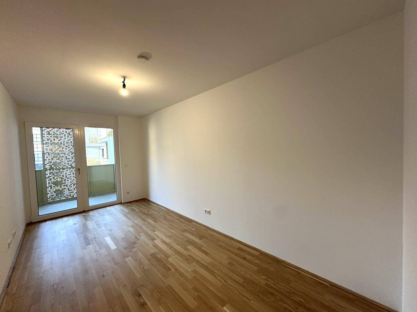 Helles Zimmer mit Parkettboden und Balkonzugang, ideal als Schlaf- oder Arbeitszimmer.