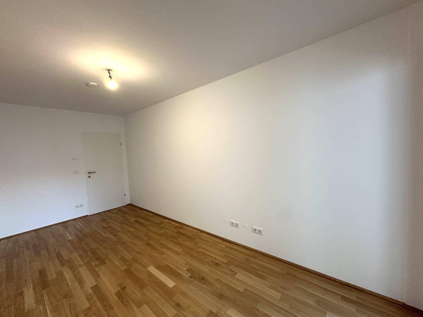 Leeres Zimmer mit Parkettboden und weiß gestrichenen Wänden, bereit zur individuellen Gestaltung.