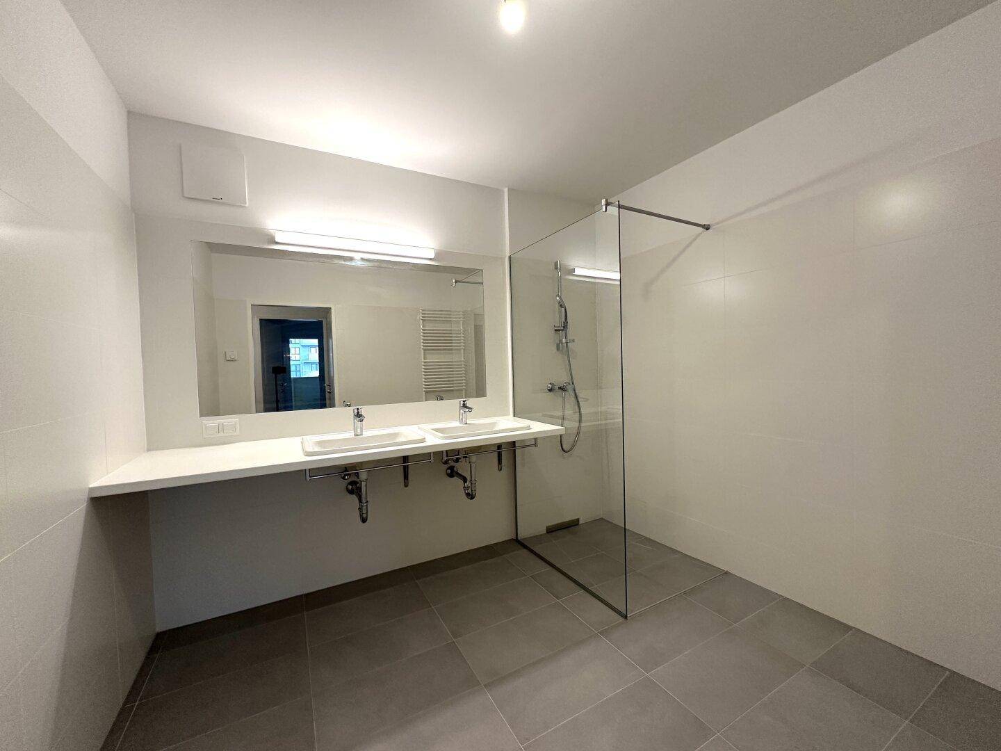 Modernes Badezimmer mit Doppelwaschbecken, großer Dusche und hellen Fliesen.