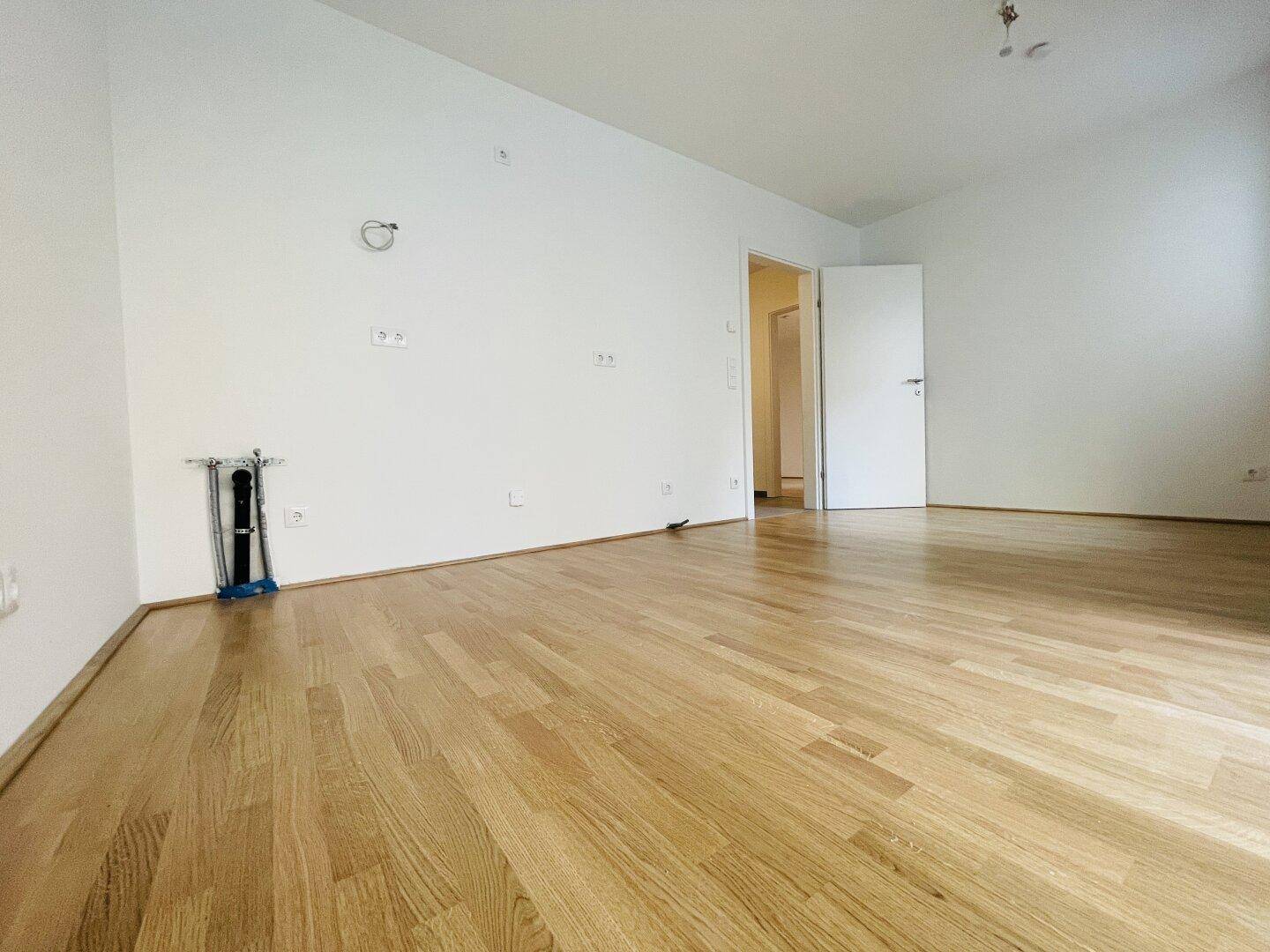 Helles, leeres Wohnzimmer mit hellem Parkettboden und weißen Wänden, bereit zur Einrichtung.