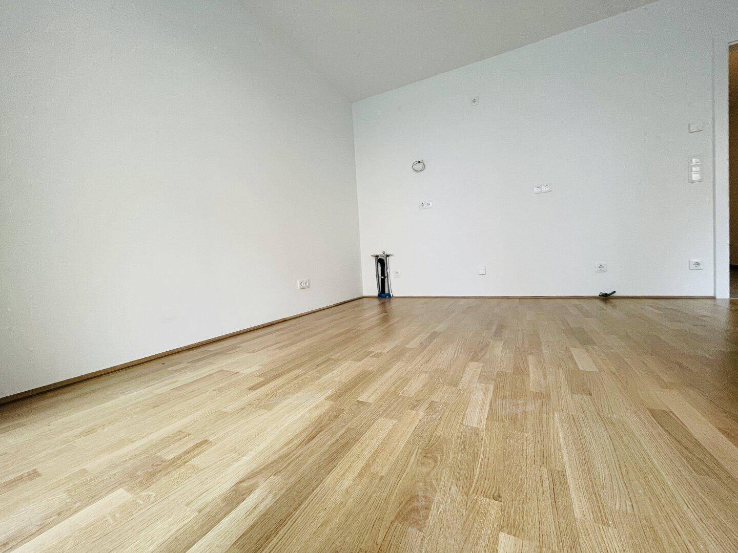 Geräumiges, leeres Wohnzimmer mit hellem Parkettboden und weißen Wänden, ideal für individuelle Gestaltung.