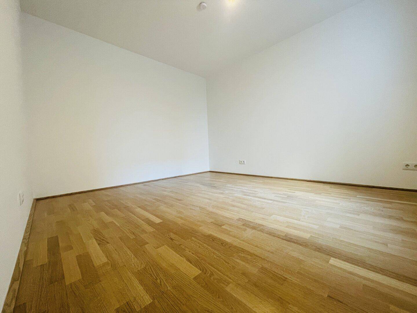 Leeres Schlafzimmer mit hellem Parkettboden und weißen Wänden, bereit zur individuellen Gestaltung.