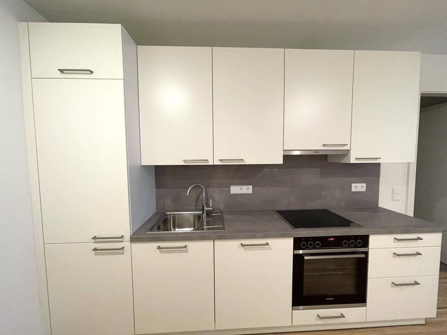 Moderne Einbauküche mit weißen Schränken, Induktionskochfeld und Backofen.