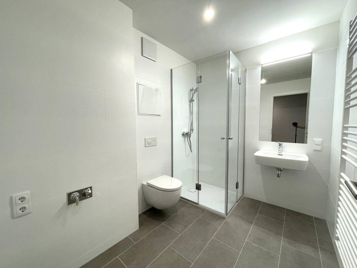 Modernes Badezimmer mit Dusche, wandhängendem WC und Handtuchheizkörper.